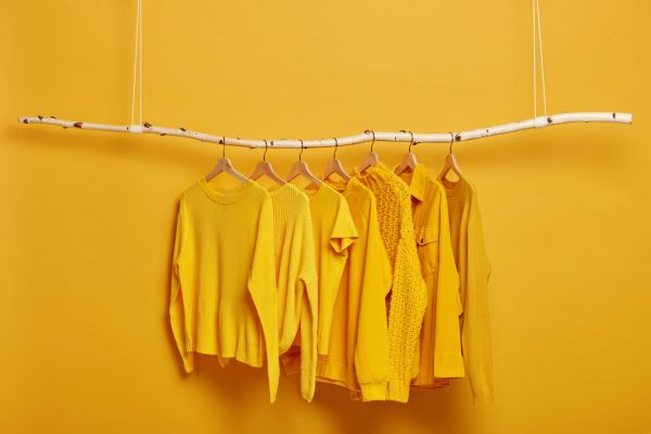 Collection of plain yellow sweaters and jackets for women hanging on rack in dressing room. Selective focus. Fashionable winter or autumn clothes. Sale in fashion store. Dressing closet with clothing